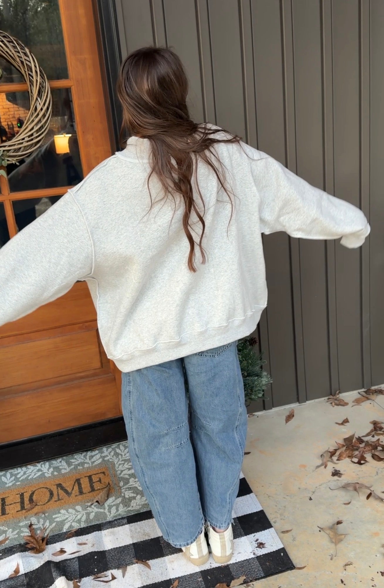 Person wearing a white sweater and blue jeans standing on a porch with a 'Home' sign in the background.