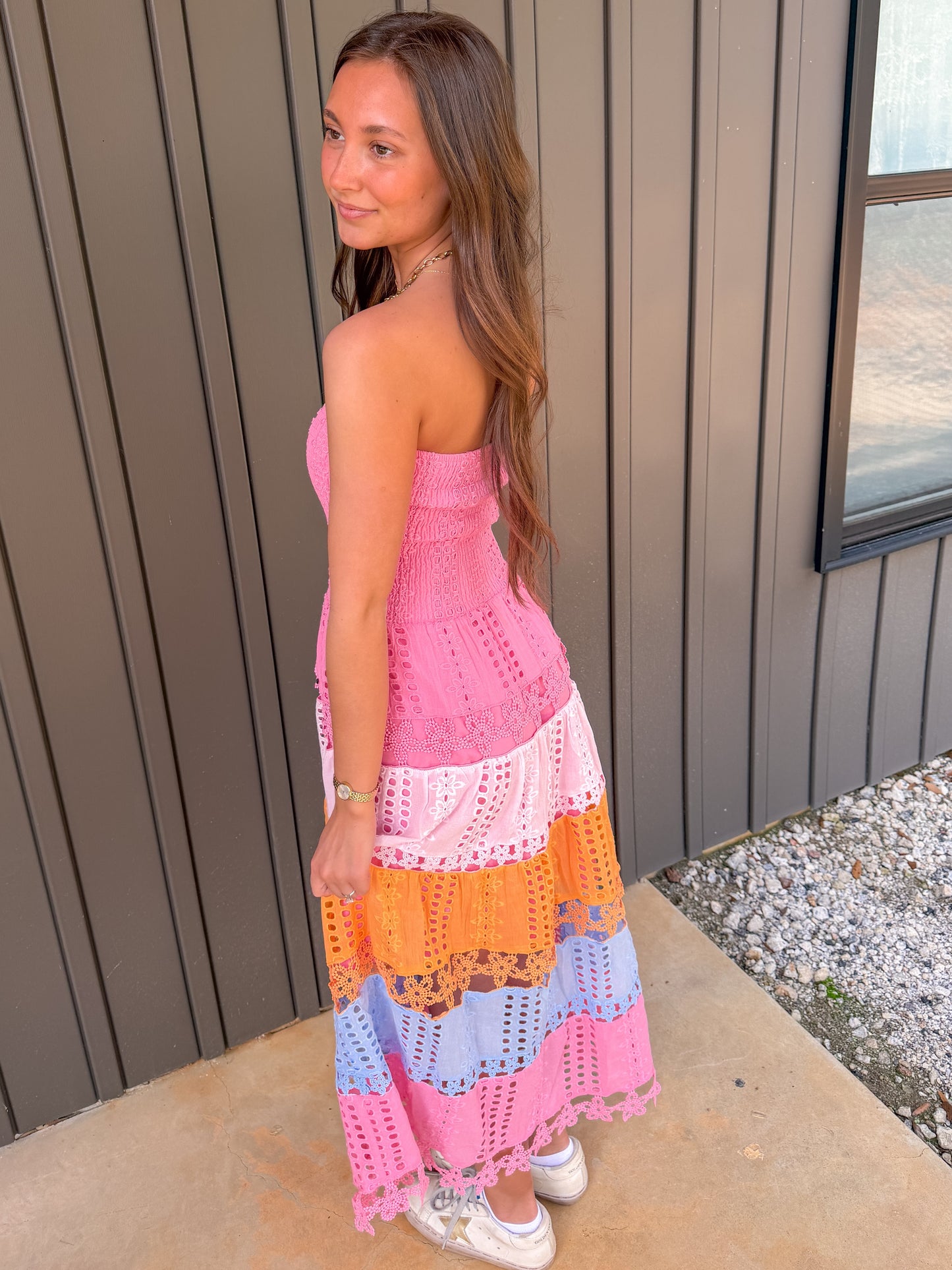 Woman wearing a colorful crochet dress standing against a neutral wall.