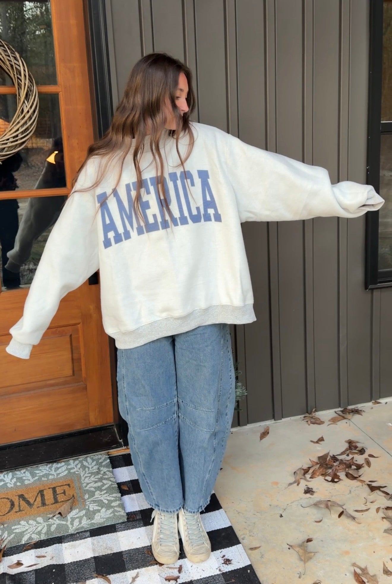 Person wearing a white sweatshirt with 'AMERICA' printed on the back, standing in front of a house entrance.
