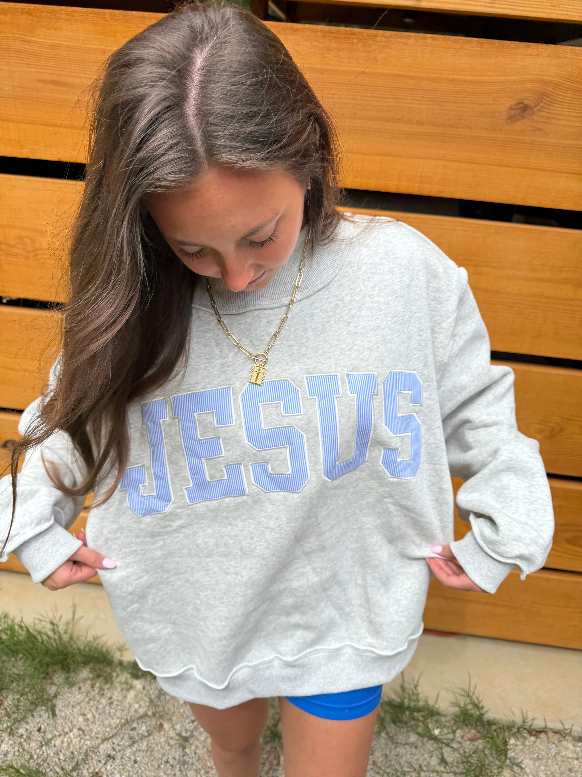 Person wearing a white sweatshirt with 'JESUS' printed on it, sitting on a wooden bench.
