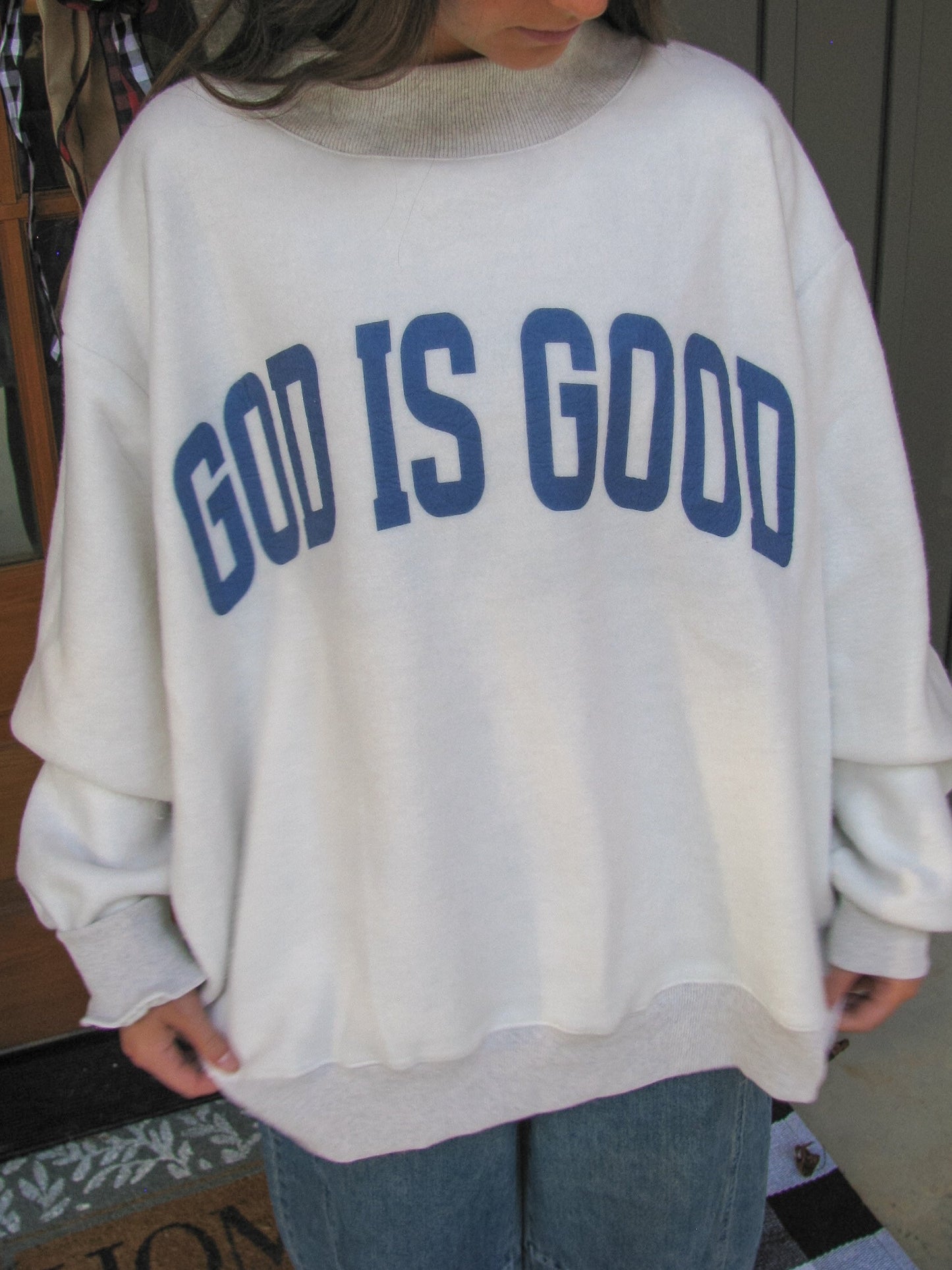 Person wearing a white sweatshirt with 'GOD IS GOOD' text in blue.