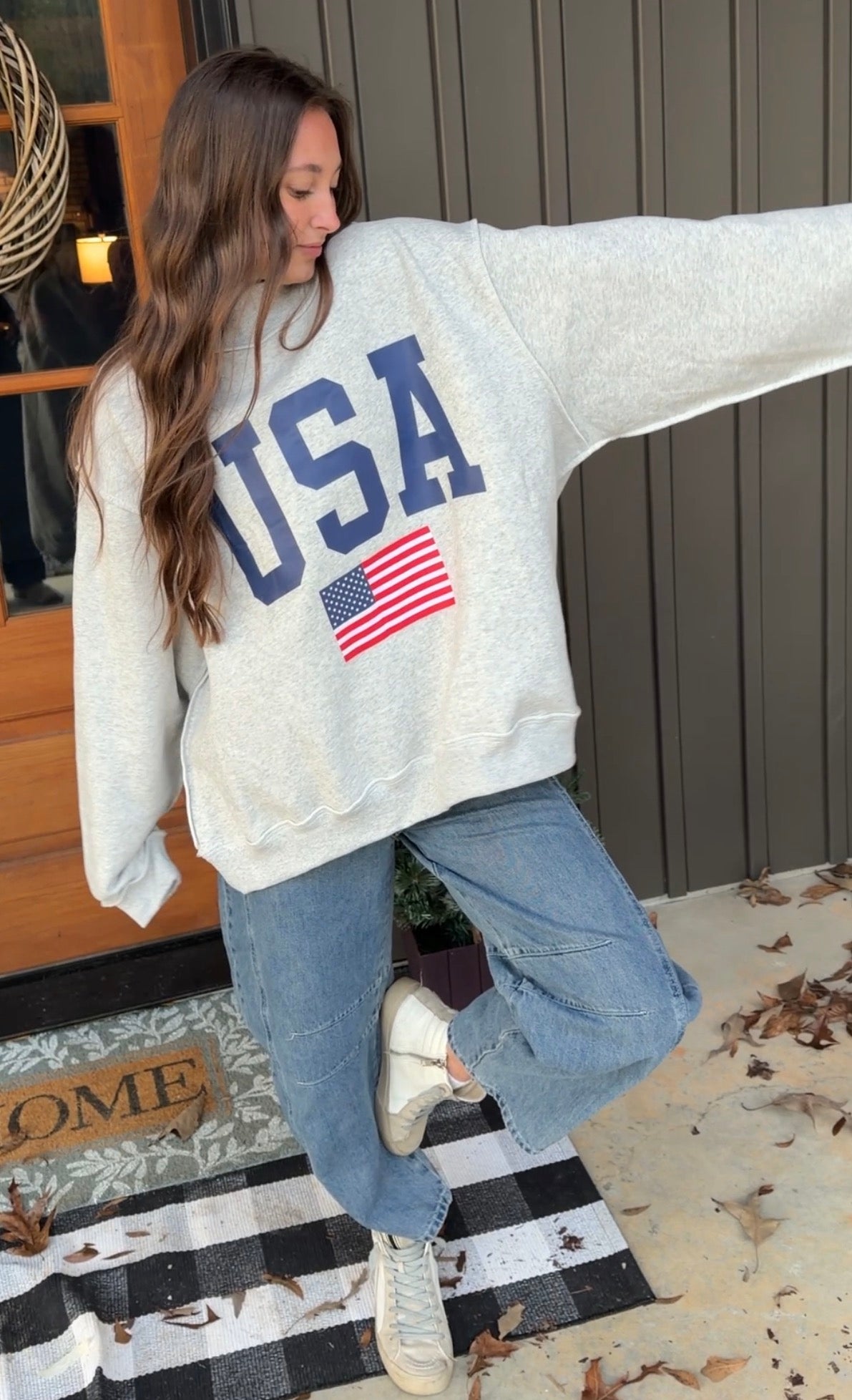 Woman wearing a white sweatshirt with 'USA' and an American flag design, standing on a checkered floor.