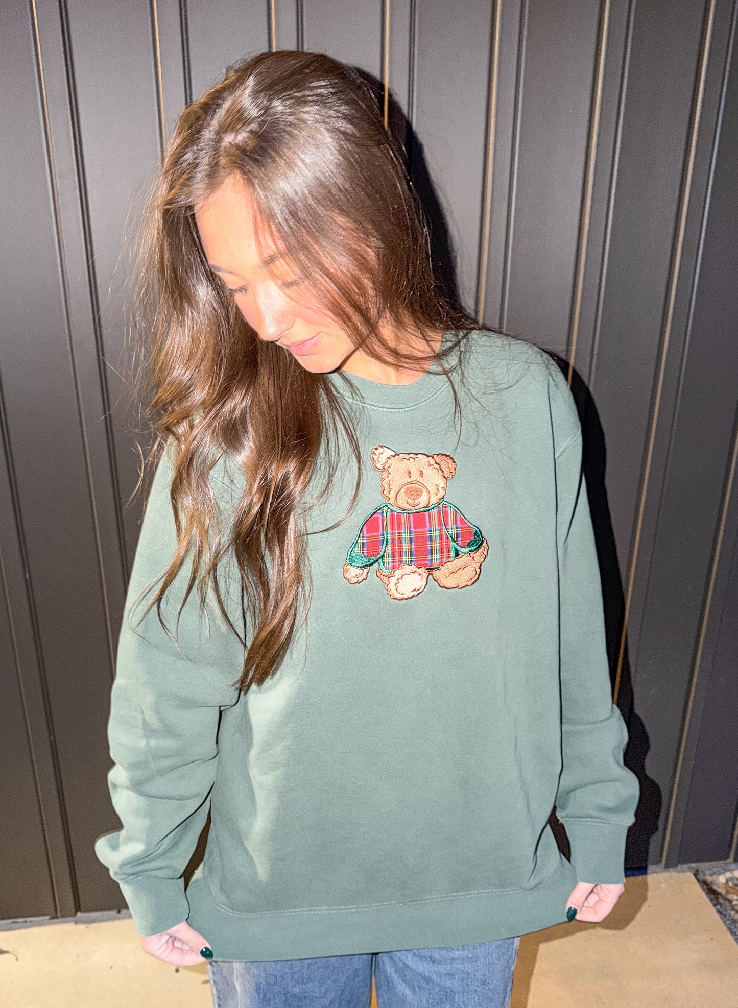 Person wearing a green sweatshirt with a teddy bear design against a wooden panel background