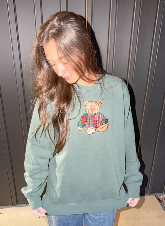 Person wearing a green sweatshirt with a teddy bear design against a wooden panel background