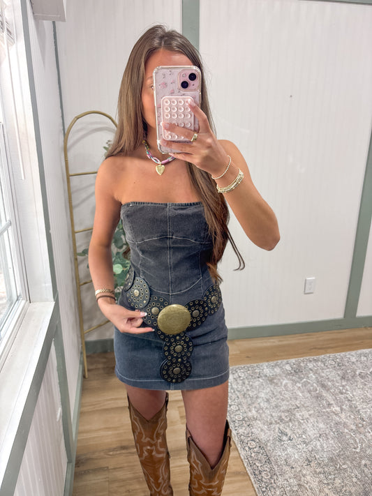Woman taking a mirror selfie wearing a 
black denim dress with embellishments and brown knee-high boots going to country concert