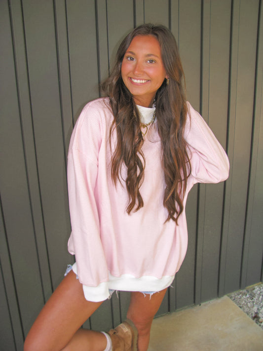 Woman wearing a pink stripe mock neck sweatshirt and  against a wooden wall.